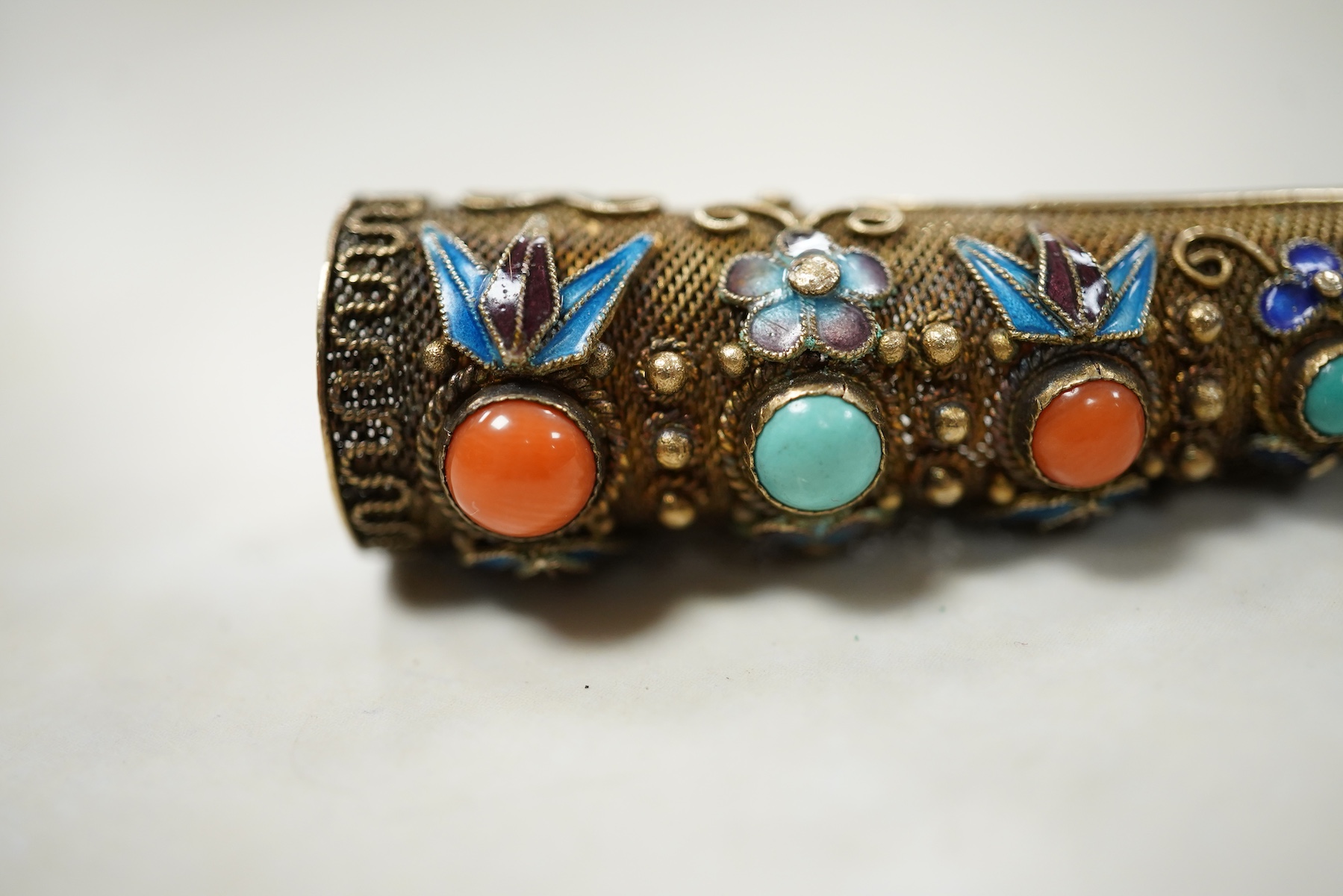 A Chinese silver gilt coral and turquoise nail guard brooch, composed of filigree, set with coral and turquoise cabochons, applied with foliate designs in blue enamel, length 8.4cm, stamped SILVER, Condition: in good con
